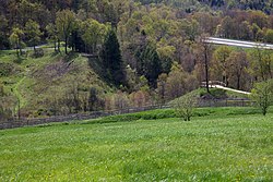 A modern view of the South Fork Dam. The large gap overlooked by the two wooden terraces pictured is the breach that caused the Johnstown Flood.