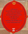Plaque rouge ovale indiquant : « En mémoire du "District Officier" Charles Pearson de la "London Fire Brigade" qui est mort de ses blessures au numéro 100 Sidney Street, proche de ce site pendant le Siège de Sidney Street, le 3 janvier 1911 ».