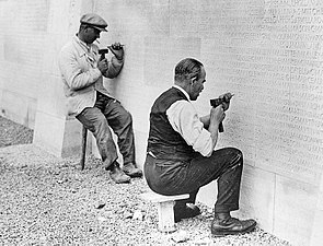 Dois homens gravando nomes em um lado do Memorial do Canadá em Vimy.