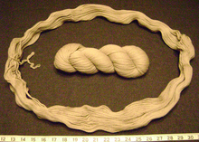 A hank of wool yarn (center) is uncoiled into its basic loop. A tie is visible at the left; after untying, the hank may be wound into a ball or balls suitable for knitting. Knitting from a normal hank directly is likely to tangle the yarn, producing snarls. Yarn hank uncoiled.png