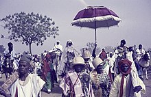 Ceremonial ruler of Bauchi under a red-white parasol on a white horse, 1970-1973. ASC Leiden - Rietveld Collection - Nigeria 1970 - 1973 - 01 - 069 Sallah festivities in Bauchi. Group outside in white, red and green. Riders on camel and horse, red-white parasol for the ceremonial ruler of Bauchi.jpg