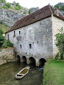 Photo d'une grande bâtisse en pierre de taille reposant sur quatre arches romanes en travers de la rivière.