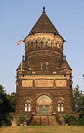 Monument in gotische stijl in bruine steen.  De eerste verdieping is vierkant en wordt bekroond door een cilindrische tweede verdieping en een kegelvormig dak.