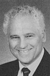 Black-and-white photo of a man with a wide smile and short curly hair wearing a light-colored suit