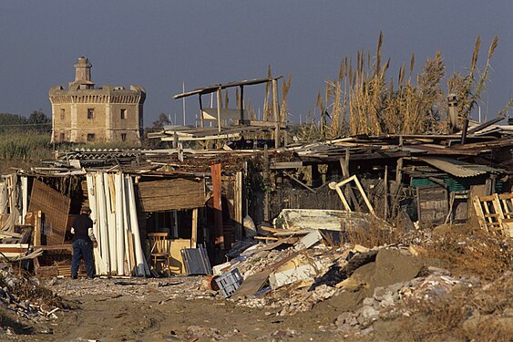 Ostia ponente nel 1990; duna costiera ridotta a discarica e baracche nei pressi della spiaggia, sullo sfondo la Torre S.Michele