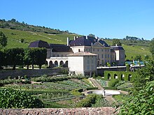 La photo couleur représente un château devant lequel s'étend un jardin à la française. En arrière-plan, le coteau est couvert de vignes.