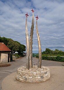 Stone base with three gently twisting steel trails rising upwards, each topped with a red glass aircraft