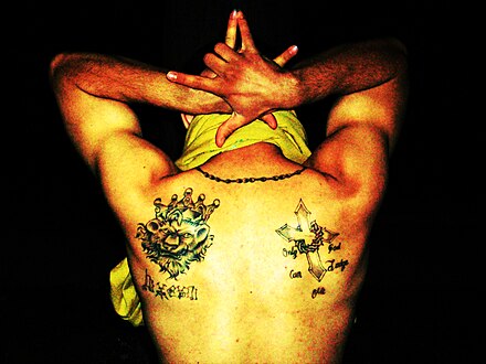 Latin King gang member showing his gang tattoo, a lion with a crown, and signifying the 5 point star with his hands