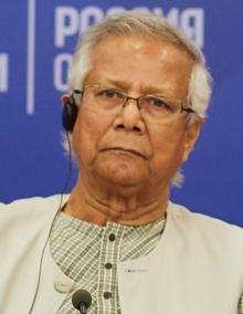 Yunus speaking at a panel in the Our Future foundation. He is a middle-aged man with glasses wearing a white suit.