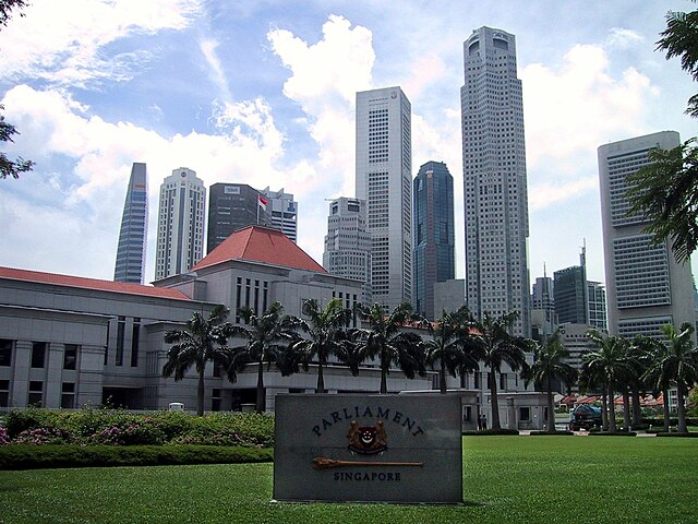 Large white building with a red roof, with a palm-lined path leading up to the main entrance