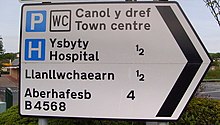 A Welsh-English bilingual sign in Newtown, Powys, with Welsh first, then English, and also Welsh place names without an English equivalent. Distances in miles. Welsh spelling on road sign, Newtown, Powys - geograph.org.uk - 1319438 (cropped).jpg