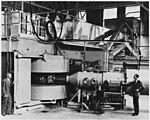 Gambar hitam-putih alat berat dengan dua operator duduk di samping