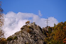 Kamenná mohyla se zříceninou hradu. Napravo od ruiny je elektrický pylon.