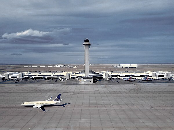 The Air Traffic Control Tower and Concourse C at Denver International Airport with a United Airlines Boeing 737-800 taxiing below