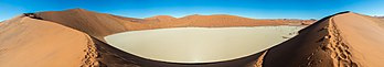 Vista superior de Sossusvlei, Namíbia. Sossusvlei (às vezes escrito Sossus Vlei) é um lago seco, de forma quase elíptica, coberto por uma crosta de areia rica em sal. Embora a bacia tenha sido moldada ao longo do tempo pelo rio Tsauchab, a inundação real da bacia é um evento relativamente raro, e às vezes vários anos se passam entre uma enchente e a próxima. O rio fica seco a maior parte do ano e, mesmo quando não está, carrega relativamente pouca água para o lago. Este é cercado por dunas altas alaranjadas, parcialmente cobertas por uma vegetação composta por gramíneas, arbustos e algumas árvores (principalmente da espécie Vachellia erioloba). (definição 31 438 × 5 482)