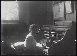 Unidentified woman sat at desk with computing machine. A framed pencil sketch of Francis Galton hangs on the wall above the desk. Galton Laboratory 1.jpg