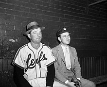 Jack Kent Cooke (right) swaps hats with Joe Becker, who managed the Leafs in 1951-52. Jack Kent Cooke with baseball player in Toronto Maple Leafs Baseball Club dugout, Maple Leaf Stadium.jpg