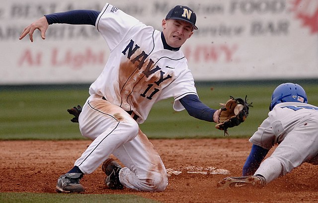 A shortstop tries to tag out a runner who is sliding head first, attempting to reach second base.