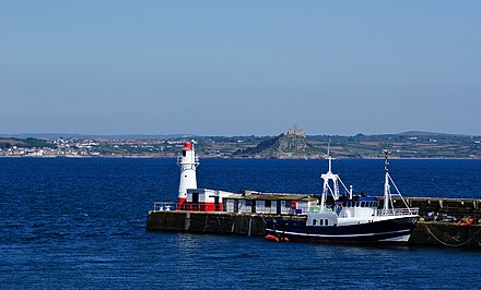 View from Newlyn Harbour showing the lighthouse and Tidal Observatory to its right, both painted red and white.