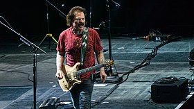 Johnston interpretando um Top de ouro do artista Paul Reed Smith enquanto vestia uma camiseta preta e jeans, em frente às coloridas luzes do palco