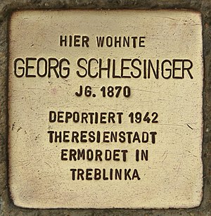 Goldfarbener, quadratischer Stolperstein. Aufschrift in Großbuchstaben: Hier wohnte Georg Schlesigner Jg. 1870 Deportiert 1942 Theresienstadt Ermordet in Treblinka