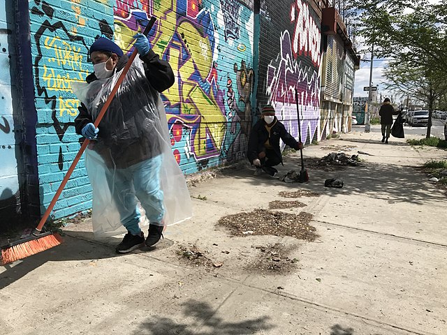 Dirt-covered sidewalk in Brooklyn, NYC being swept during a community clean-up