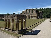 Fotografia di alcuni portici romanici che formano l'angolo di un chiostro, tutto il resto di quest'ultimo scomparso;  sullo sfondo, rovine più importanti.