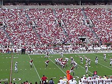 Alabama se postaví k útoku a Arkansas k obraně na hřišti amerického fotbalu s velkou korunou v hledišti.