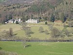 a country house in parkland between a river in the foreground and a forest in the background