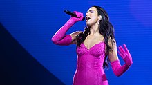 Photographie de Dua Lipa, vêtue de rose, chantant sur scène lors d'un concert de 2022.