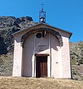 Photographie d'une chapelle en contre-plongée avec vue sur son clocher métallique et sa porte en bois.