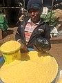 A young man at an outdoor market stall sells a kind of flour made from cassava called garri