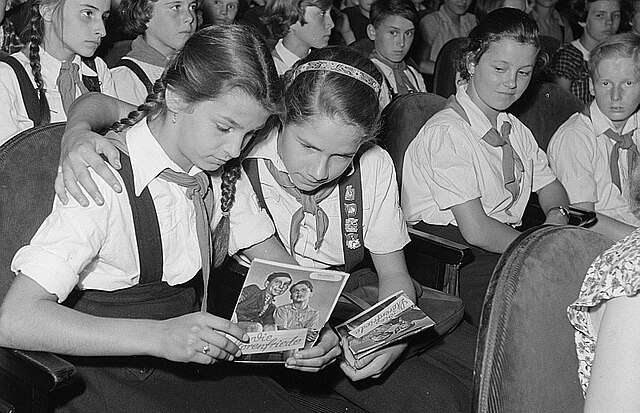 Two Young Pioneers examine the brochure for the DEFA children's film Die Störenfriede (The Trobulemakers) before a screening, July 1953