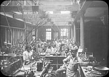View of the production floor, circa 1911. Kapp & Peterson- Men-women pipe making (19909756014).jpg