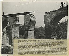 Vue en plongée du pont dynamité, deux arches sont manquantes, le tablier temporaire est en cours d'installation, reposant sur uniquement deux piles du pont.