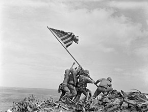 Four soldiers plant a U.S. flag on a long pole on a bare mountaintop