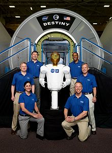The Robonaut2 and STS-133 crewmembers pose for a picture near a Destiny lab trainer. (The photo includes original crew member Tim Kopra, who was later replaced by Stephen Bowen).
