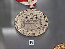 Photo d'une médaille sur laquelle on peut voir le logo des Jeux et les mots « Olympische Winterspiele XII Innsbruck 1976. »