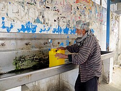 An elderly man fills a water container at a public multi-faucet sink in Khan Younis, Gaza Strip. Water supply in West Bank and Gaza February 2014 2water photoblog.jpg