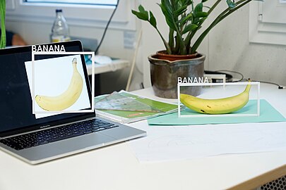 The artist has put a banana on a table and the image of a banana on the screen of a laptop, framed both of them, and labeled them