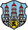 Barevná reprodukce městského znaku s motivem hradby a tří věží, v dolní části je štít se lvem