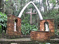 Каменен олтар с две изображения на християнски светци в градина и върху него лък, носещ кръст