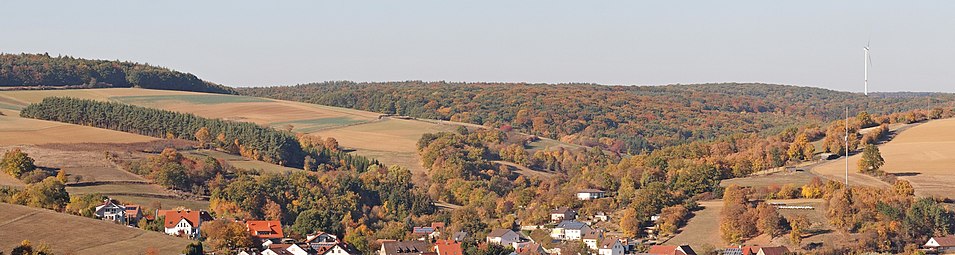 Blick über Hausen auf den westlichen Teil des Naturschutzgebietes Hausener Talhänge, der entlang des Hesselbacher Grundes verläuft (vor dem Wald mit Windrad)