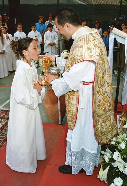 Catholic priest in Sicily distributing the Eucharist to a child at her first Holy Communion