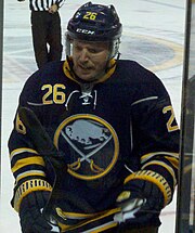 A closeup of an ice hockey player focusing on his head and shoulders. He is looking to the right and is wearing a black helmet and a blue uniform.