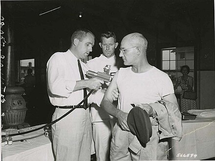 SP5 Lawrence E. Blackman (Darlington, SC) Hq & Hq Co, USASTC, receives the first typhus shot administered by a jet injector at Fort Gordon by Mr. John R. Gordon, representative of the R.P. Scherer Corp., Detroit, Michigan, August 1959.