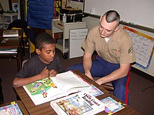 A U.S. Marine helps a student with reading comprehension as part of a Partnership in Education program sponsored by Park Street Elementary School and Navy/Marine Corps Reserve Center Atlanta. The program is a community outreach program for sailors and Marines to visit the school and help students with class work. US Navy 021211-N-4528H-004 Partnership in Education Communitee Program.jpg
