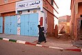 A man in black dress before a shut telephone booth in Dakhla.jpg