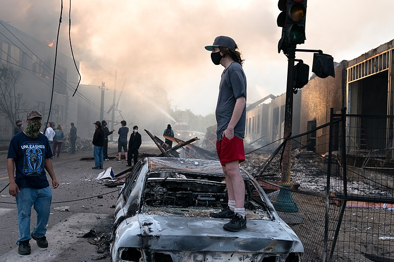 Datei:A man stands on a burned out car on Thursday morning as fires burn behind him in the Lake St area of Minneapolis, Minnesota (49945886467).jpg