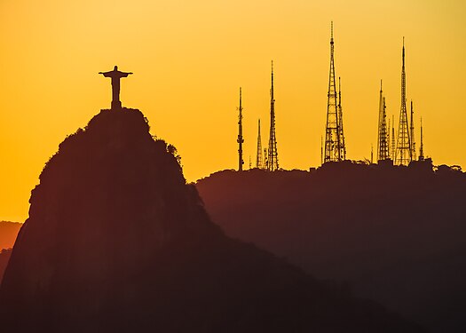 Modern transmission towers overshadow Rio de Janeiro’s iconic Christ the Redeemer statue. View is from Sugarloaf Mountain during sunset.